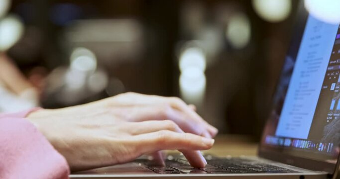 This close-up shot depicts the hands of a young woman working with a computer in a café. As she types on the keyboard, her hands move swiftly and confidently