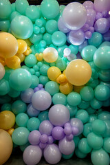 A wall hung with a lot of colorful balloons, purple, green and yellow. The balloons are arranged in different sizes and positions to create a visually vibrant scene.