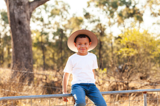 Portrait of a first nations Australian boy smiling and sitting on gate in a paddock