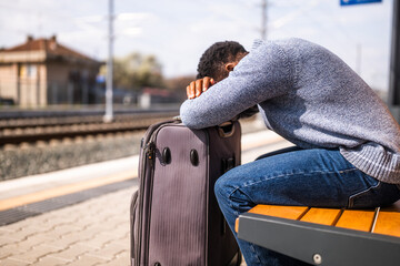 Worried man with a suitcase sitting on a bench at the railway station. - 765635142