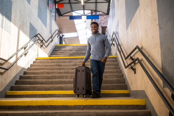 Happy man with suitcase walking down a stairs in railway station. - 765635303