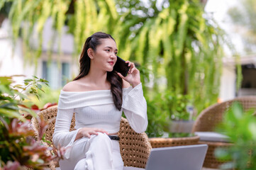 Cheerful young woman having fun conversation on smartphone while sitting at outdoor cafe with laptop.