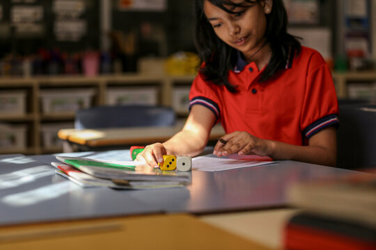 girl student at her desk working on maths problems using dice