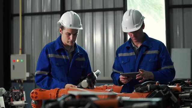 Factory workshop: professional male engineer Male machine operator uses an industrial digital tablet computer to operate and program a robot arm for the production line. High tech facilities with mach