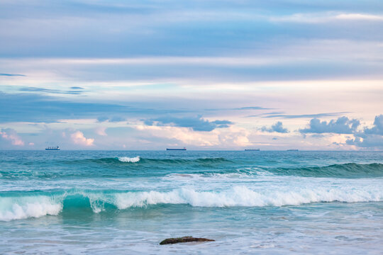 Cargo ships lined up at sea on their way to Newcastle Harbour under a vibrant sunset sky