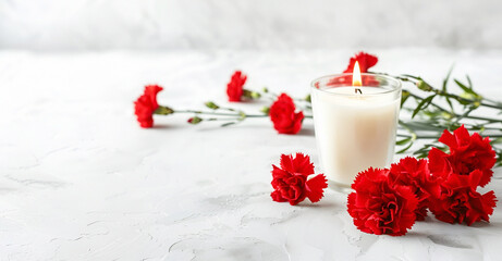 A white candle with red carnation flowers on a white table