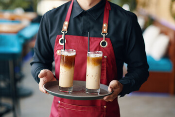 Cropped image of waiter holding tray with glasses of iced coffee