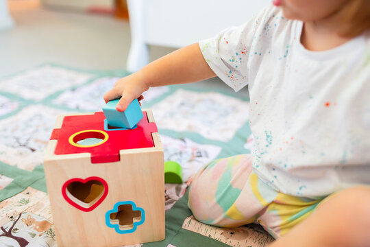 Toddler posting coloured shapes into wooden shape sorter box