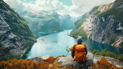 Behangcirkel Traveler with backpack gazes at lake from rock in natural landscape © AlexanderD