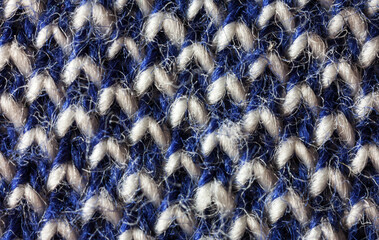 Close-up of a variegated hand-knitted wool fabric with geometric pattern. Natural blue and white wool textile background. Warm woolen cozy clothes. Flat lay, macro, top view, mockup