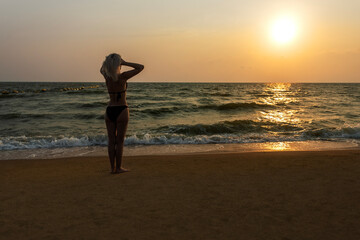  Caucasian woman in bikini swimsuit standing on the beach and enjoying sunset. people, summer vacation and leisure concept