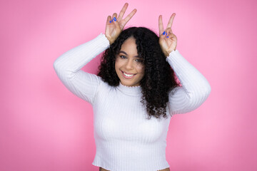 African american woman wearing casual sweater over pink background Posing funny and crazy with fingers on head as bunny ears, smiling cheerful