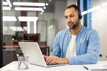 Serious young Muslim man wearing a headset is concentrating on working on a laptop while sitting at...