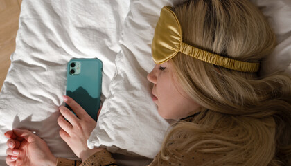 Woman asleep with phone, wearing eye mask