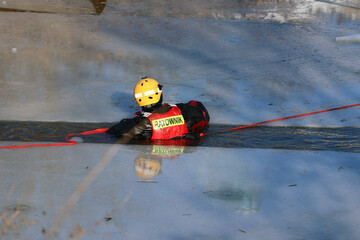 Ratownik wodny w zimie na lodzie ratuje topielca.  - obrazy, fototapety, plakaty