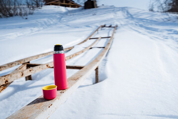 A pink thermos and cup rest on a wooden bench in the freezing snow