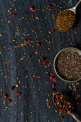 Old spoons with various seeds and spices on black background