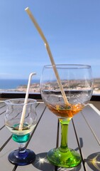 Pair of cocktail glasses with biodegradable straw, on panoramic sea view background.  Aperitif with friends.  Outdoor fun.Romantic meeting for two. Couple's anniversary. Work break.