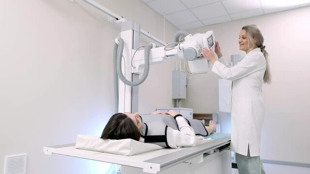 A female doctor installs an x-ray machine and prepares a young patient for the procedure. Scans and treats fractures, broken limbs, injuries, cancer or tumors. Modern Hospital