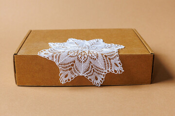 A thin delicate napkin knitted with knitting needles lies on a kraft cardboard gift box on a brown...