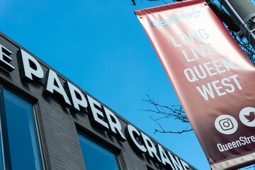 Fototapeta premium projecting banner sign celebrating Queen Street West (and building sign for the now closed The PaperCrane & Co located at 224 Queen Street West) in Toronto, Canada