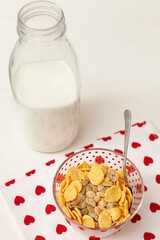 Tasty corn flakes with granola in bowl with bottle of milk. Rustic background with beautiful napkin with heart print. Healthy crispy breakfast snack. The concept of a healthy lifestyle. - 765692589