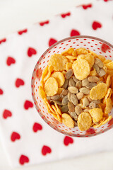 Top view on tasty corn flakes with granola in bowl. Rustic background with beautiful napkin with heart print. Healthy crispy breakfast snack. The concept of a healthy lifestyle. - 765692794