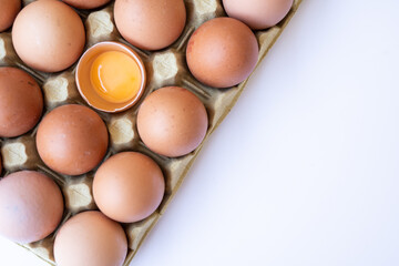 Fresh chicken brown eggs in a tray on a white background. Broken egg with yolk inside the shell.
