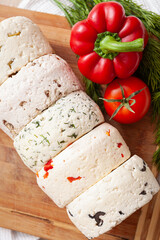Closeup of several varieties of homemade cheese with different fillings with paprika, dill, olives, walnuts and cookies on a wooden board with fresh dill, tomatoes and bell pepper. - 765693900