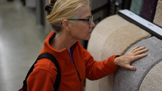 Attractive mature woman shopping for carpet looking through samples for home redecorating project, in a hardware store.