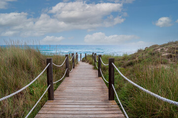 Wooden footbridge between sand dunes to the beach and ocean at menorca spain