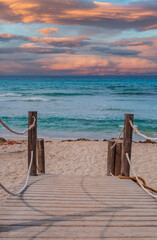 Wooden bridge to the beach and ocean at menorca spain with sunset