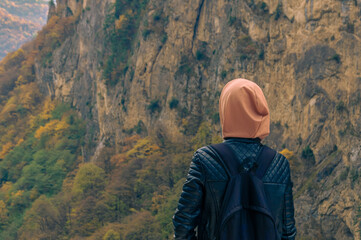 A girl in a black jacket and a pink hood looks at the gorge. A walk in the mountains. Walking and traveling in the highlands. The girl looks at the mountains.