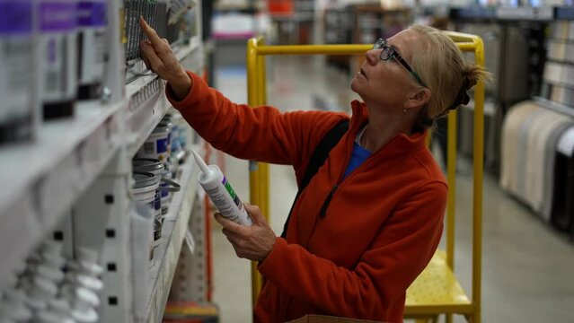 Woman looking at tubes of caulk in a hardware store, comparing products. Concept of home remodeling shopping experience.