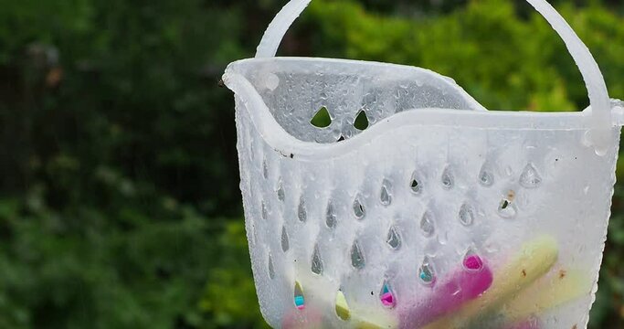 A short film clip in full HD of a translucent plastic basket swinging in the wind on a rainy day. No