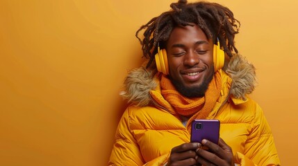 A man wearing glasses and a yellow sweater is smiling while holding a cell phone