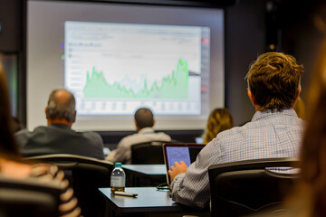 A person attending a seminar on stock market investing, gaining knowledge about business and investing to increase returns