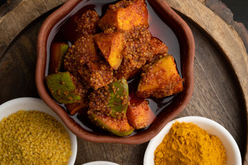 Homemade Mango Pickle or aam ka achar Kairi Loncha stored or preserved in China clay pot with Ingredients.