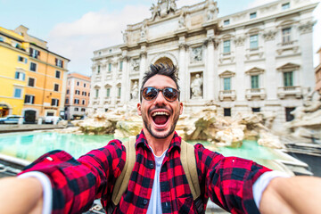 Happy young tourist taking selfie in front of Trevi Fountain during summer vacation in Italy - Happy man enjoying summertime holiday in Europe - Travel and technology life style concept - obrazy, fototapety, plakaty