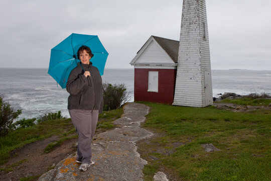 A woman is walking on a path near a lighthouse and holding a blue umbrella