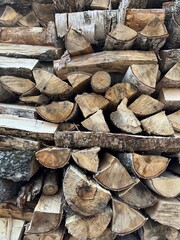 A pile of firewood is stacked. Cut down trees lie in one heap. Material for fire and heating. Birch and oak firewood, lumber.