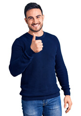 Young handsome man wearing casual clothes doing happy thumbs up gesture with hand. approving expression looking at the camera showing success.