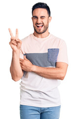 Young handsome man wearing casual clothes smiling with happy face winking at the camera doing victory sign. number two.