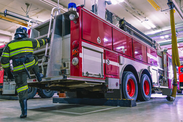 A firefighter in special clothes climbs the stairs to the roof of a fire truck. A fire truck in the...