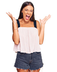 Young hispanic woman wearing casual clothes celebrating mad and crazy for success with arms raised...