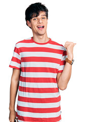Handsome hipster young man wearing casual striped t shirt smiling with happy face looking and pointing to the side with thumb up.