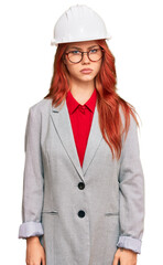 Young redhead woman wearing architect hardhat skeptic and nervous, frowning upset because of problem. negative person.