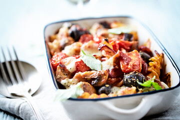 Baked pasta with cherry tomatoes, olives and mozzarella cheese. Bright wooden background. Close up. 