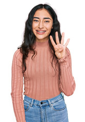 Hispanic teenager girl with dental braces wearing casual clothes showing and pointing up with fingers number four while smiling confident and happy.