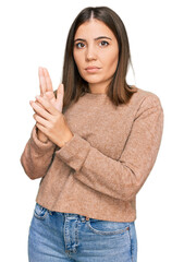 Young beautiful woman wearing casual clothes holding symbolic gun with hand gesture, playing killing shooting weapons, angry face